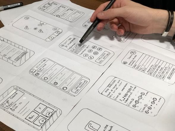 Hand-drawn mobile app wireframes being annotated with a pen